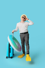 Office worker with inflatable ring, suitcase and flippers dreaming about vacation on blue background © Pixel-Shot
