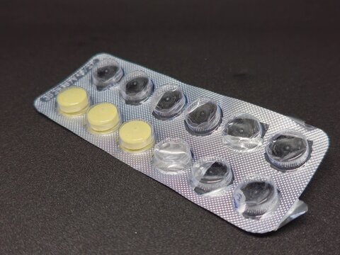 Blister pack with yellow pills and empty capsules on a dark textured surface