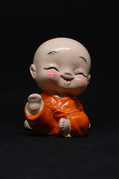 Cute ceramic figurine of a laughing baby monk in orange robes against a dark background