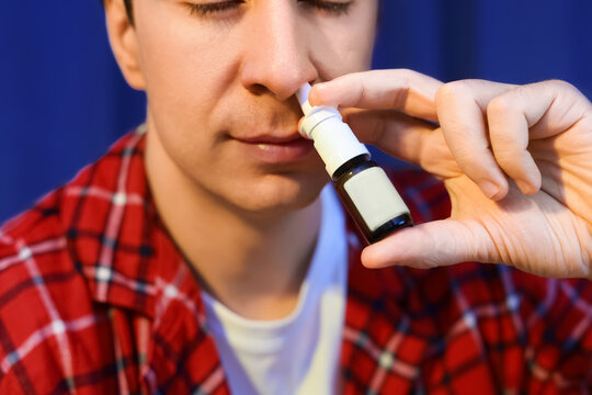 sick man using a nasal spray for cold and flu treatment. Applying medicine to his nose for allergy or respiratory illness relief.