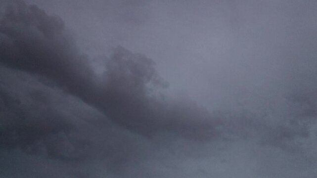 A dark gray cloud slowly moving across a pale overcast sky, creating a moody and atmospheric natural weather scene.