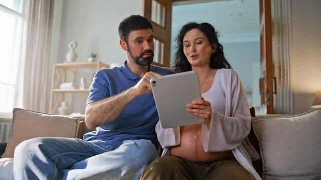 Pregnant couple relaxing sofa tablet. Happy woman husband browsing home.