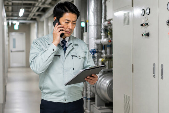 設備点検しながら電話する作業服姿の男性