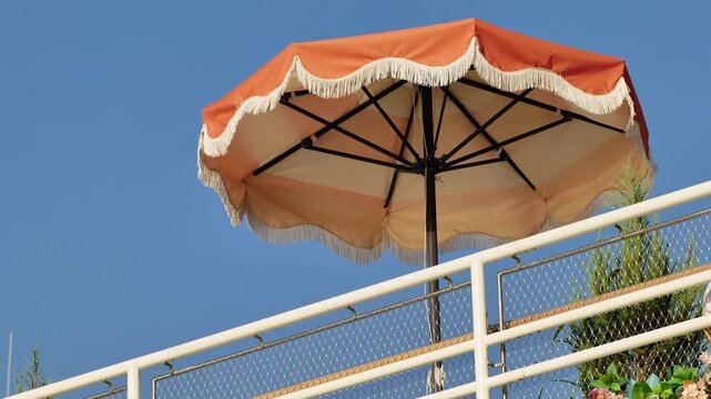 Orange umbrella with fringe against a clear blue sky on a sunny balcony