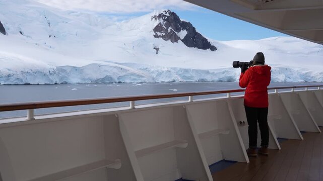 Beautiful Female Photographer Antarctica Cruise Ship Passenger in Orange Coat on Deck. Epic Adventure Travel Snow Covered Mountains Close Up.