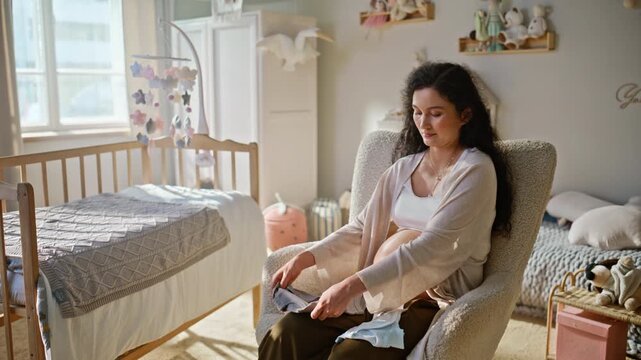 Pregnant woman inspecting baby clothes nursery. Expectant mom holding bodysuit.