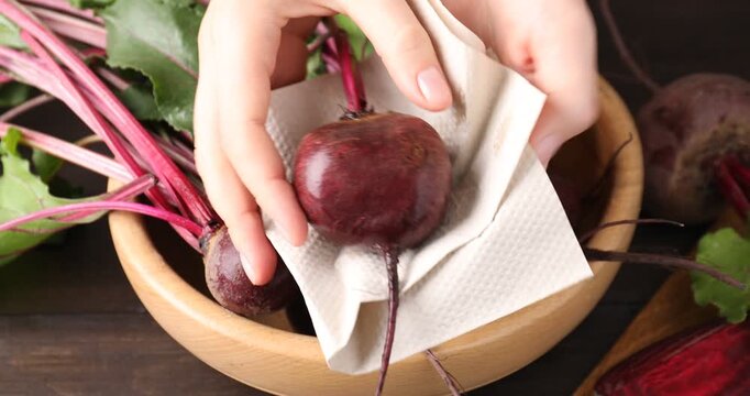 Woman wiping fresh young beet with paper towel at table, closeup