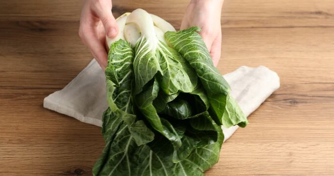 Woman with bok choi (Chinese cabbage) at wooden table, closeup