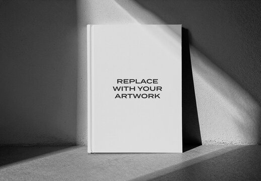 Hardcover book mockup standing upright in a corner, minimalist presentation with natural light and shadow on textured wall floor, graphic design template for cover or print media