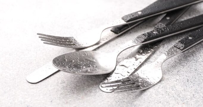 Spraying water onto stylish cutlery at gray textured table, closeup