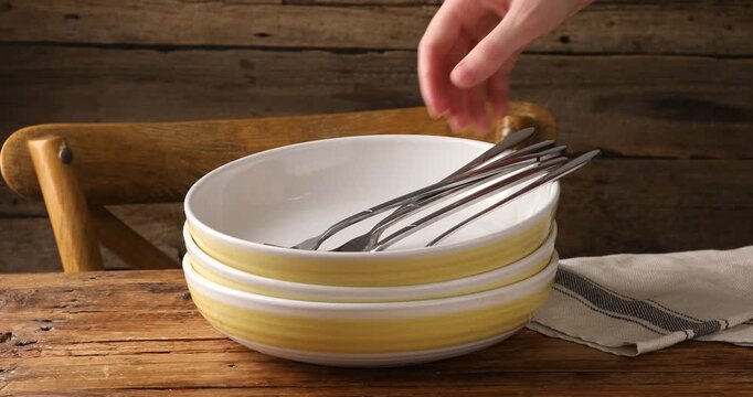 Woman putting forks into bowl at wooden table, closeup