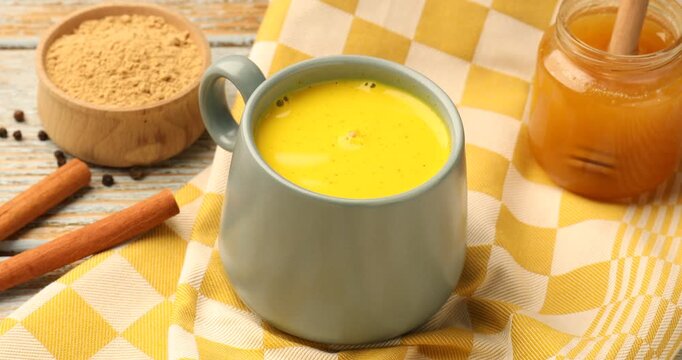Woman putting cup of golden milk turmeric latte on old wooden table, closeup