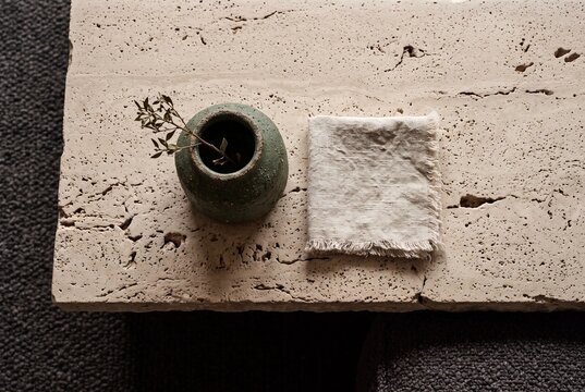 Minimalist flat lay of a rustic green ceramic vase and linen napkin on a textured travertine stone table