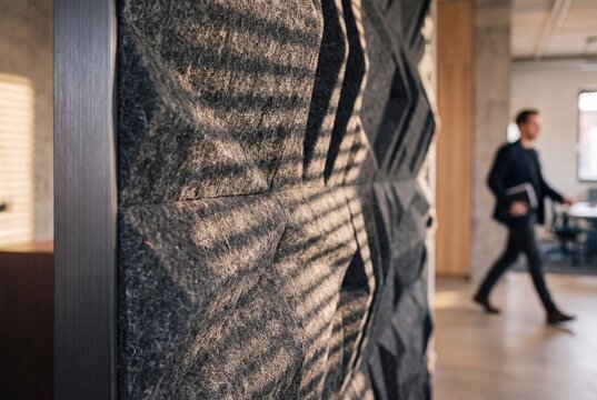 Modern acoustic wall panel with geometric texture in an open plan office with blurred businessman walking in background