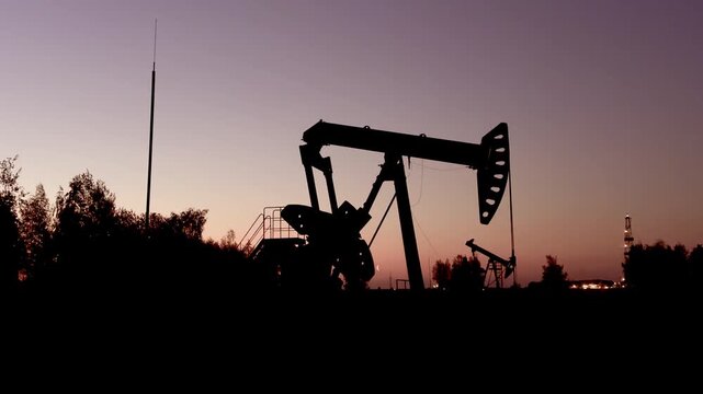 Oil extraction in oil field on evening sunset. Extraction of petroleum in night. Crude Oil Production. Crude pump jack working on oil field. Crude Pumpjack on sunrise. Industrial petroleum industry.