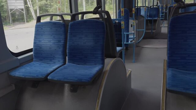 Interior of a city bus showcasing blue upholstered seats arranged in rows, with bright natural light streaming through the windows, highlighting the clean and spacious environment