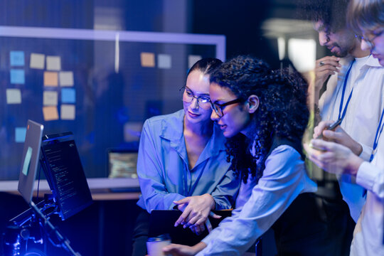 Cinematic shot of a diverse, multiethnic software team compare folder contents while standing in a modern technology office bathed in blue light, reflecting diversity and (frame 952)