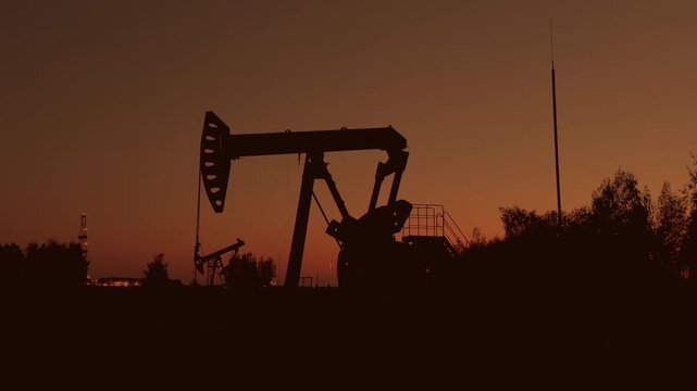 Oil extraction in oil field on evening sunset. Extraction of petroleum in night. Crude Oil Production. Crude pump jack working on oil field. Crude Pumpjack on sunrise. Industrial petroleum industry.