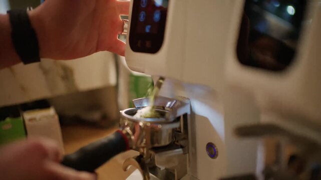 Barista grinding fresh coffee beans into portafilter using professional espresso machine.