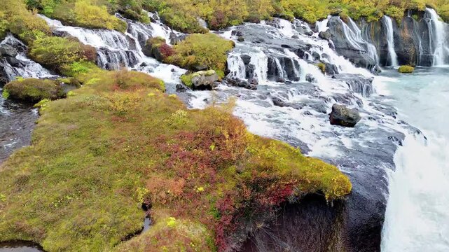 Aerial view of Barnafoss and Hraunfossar waterfalls cascading into glacial river in Iceland during autumn season.