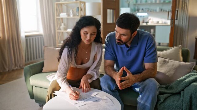 Pregnant family reviewing home budget. Wife signing papers husband explains