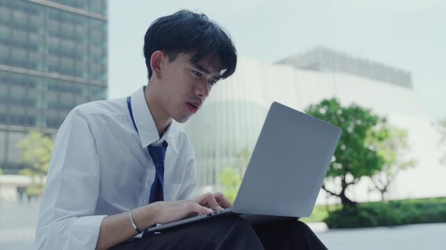 Frustrated man with laptop outdoor office work stress, sitting in city plaza under daylight pressure, young professional typing, tie loose, remote study and business task, modern glass building
