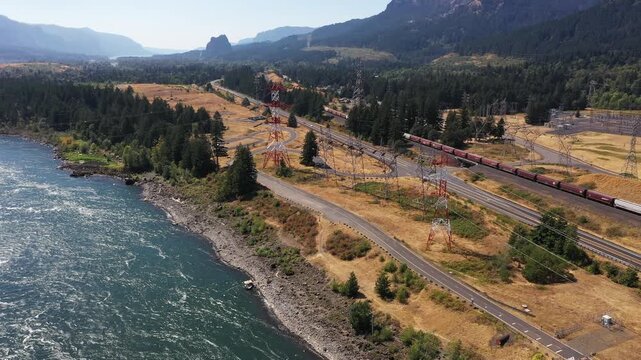 4K aerial drone footage panning over power transmission towers, Highway 14 traffic, long freight train and electrical substation near Bonneville Dam in Columbia River Gorge, Washington, USA