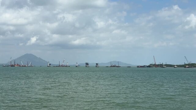 A bridge construction project spans a vast body of water, with cranes lifting the concrete bridge structure.