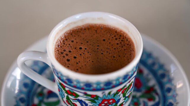 Turkish coffee served in a traditional patterned cup and saucer, showcasing its rich brown color and foamy top.