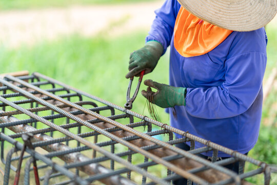 Manual worker binding steel reinforcement bars with tie wire and hand tools to assemble concrete column structures.