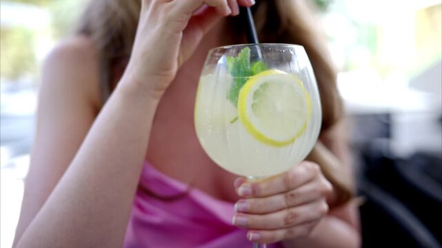Woman drinking fresh lemonade cocktail with lemon slices and mint leaves at restaurant table.