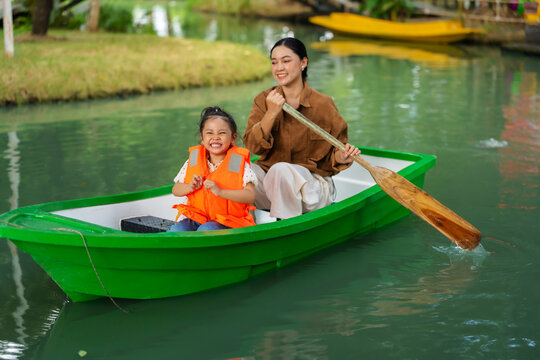 mother and preschool child girl in a green paddle boat on a scenic pond.
