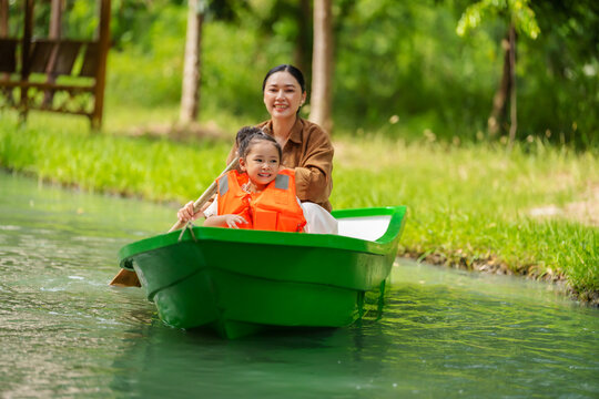 mother and preschool child girl in a green paddle boat on a scenic pond.
