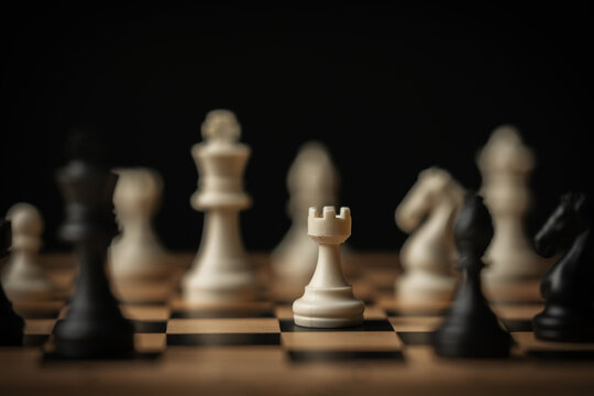 white chess rook focused on a wooden board with blurred pieces on black background