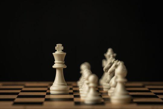 white chess king and other pieces arranged on a wooden board on black background