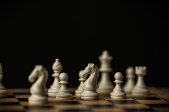 white chess knight standing on a board, surrounded by blurred pieces on black background