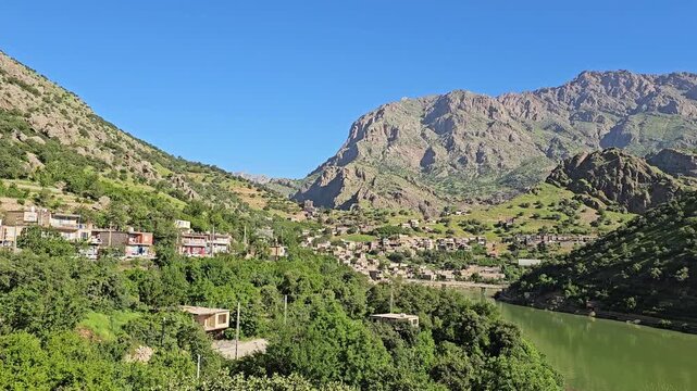 Emerald river winds past a mountain village nestled among lush hillsides, rugged peaks rising beneath a clear blue sky.
📍 Selin village, Hawraman Takht, Kurdistan 