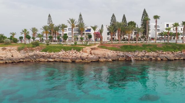 Aerial view of Mediterranean coast resort with white buildings and tropical palm trees on sunny day.