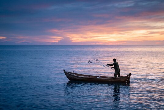 Fisherman Casting Net from Small Boat on Calm Sea at Sunset