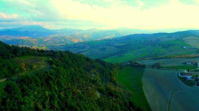 Mystical aerial truck left pan right shot from Santa Vittoria in Matenano, powerful views of the glorious Sibillini mountains, roads, meadows, thickets, hills full of vegetation, and unreal sunlight