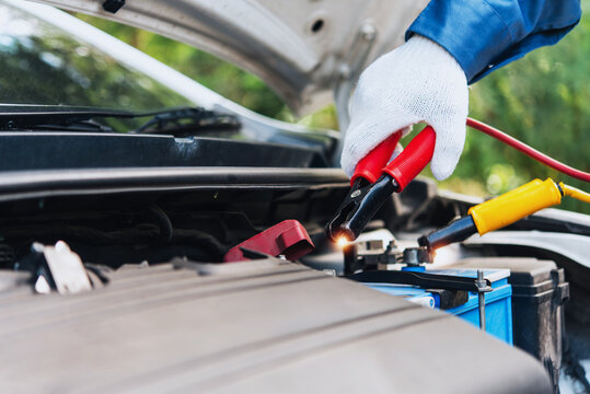 Close-up of red jumper cable clamping on dirty old car battery terminal for charging, real photography, not AI generated.