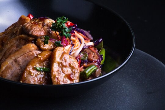 Roasted meat is served with pasta in a black bowl, accompanied by nutritious vegetables and additional greens that enhance the dish's visual appeal.