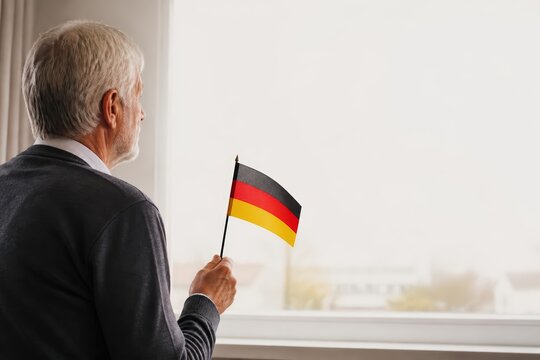 Senior man holding small German flag at window