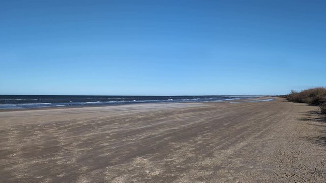 Scenic deserted beach with tranquil ocean waves gently lapping the sandy shore under a clear blue sky, showing a serene coastal landscape with no people or footprints