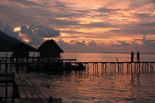 Silhouettes on wooden jetty at sunset with stilt huts, Raja Ampat, Indonesia
