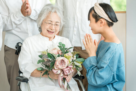 A smiling granddaughter presents a bouquet of flowers to her grandmother in a wheelchair.
