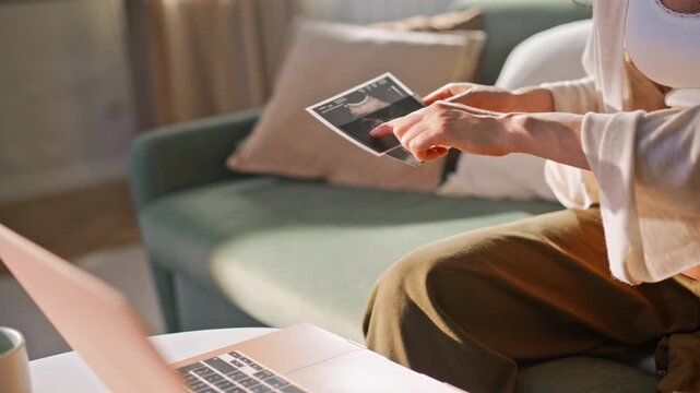 Woman holding ultrasound photo sofa. Closeup pregnant examining sonogram scan.
