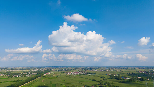 Aerial wide view of rural farmland, lake under blue sky with white clouds	
