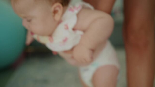 Baby wearing a diaper, with an adult helping to support its weight, practicing early motor skills and development