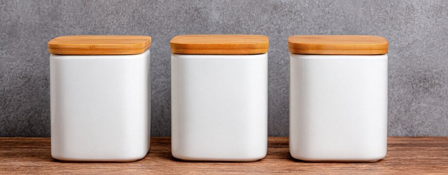 Three white ceramic kitchen canisters with bamboo lids arranged on wooden surface for minimalist food storage and home organization solutions